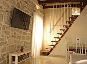 Una habitación con pared de piedra, una escalera de madera, una silla blanca y una pequeña mesa con una radio.