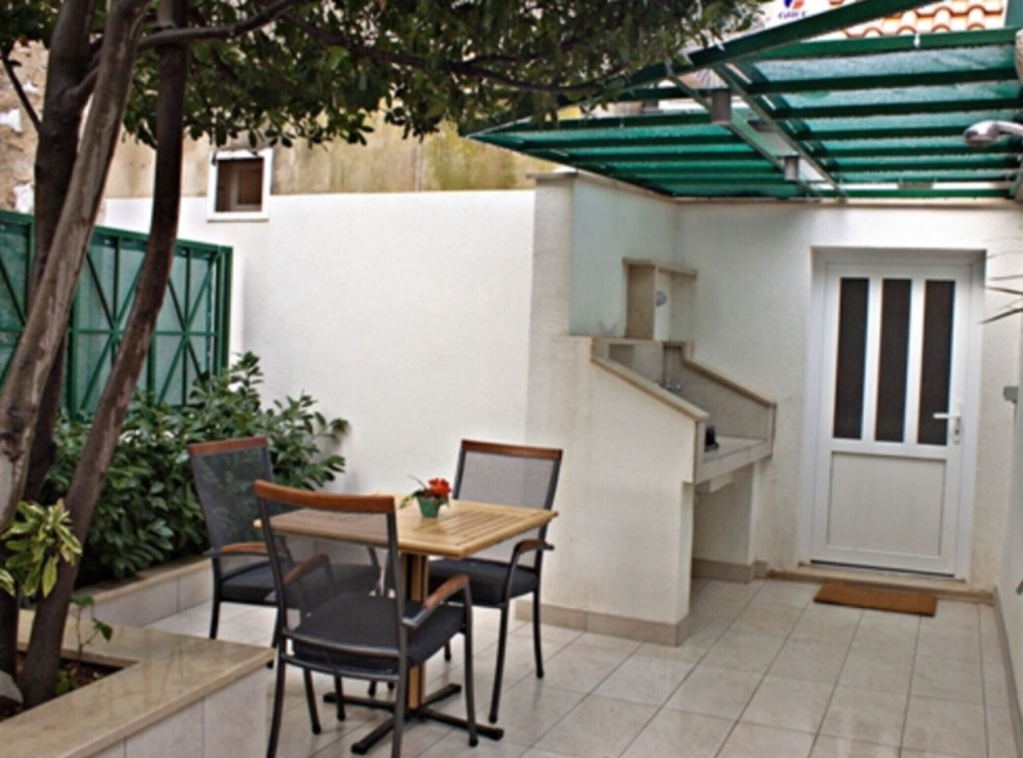 Eine kleine Terrasse mit Tisch und Stühlen, ein grünes Markise und eine weiße Tür.