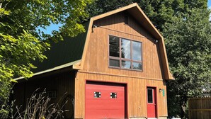Un edificio de estilo granero de madera con puerta de garaje roja, ventanas amplias y techo inclinado.