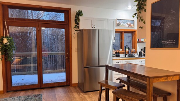 Cocina con un refrigerador grande, taburetes de madera y vistas a una terraza nevada a través de puertas de vidrio.