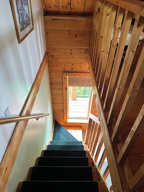 Un escalier en bois muni d’une rampe, menant à une pièce dotée d’une fenêtre et d’un tableau encadré accroché au mur.