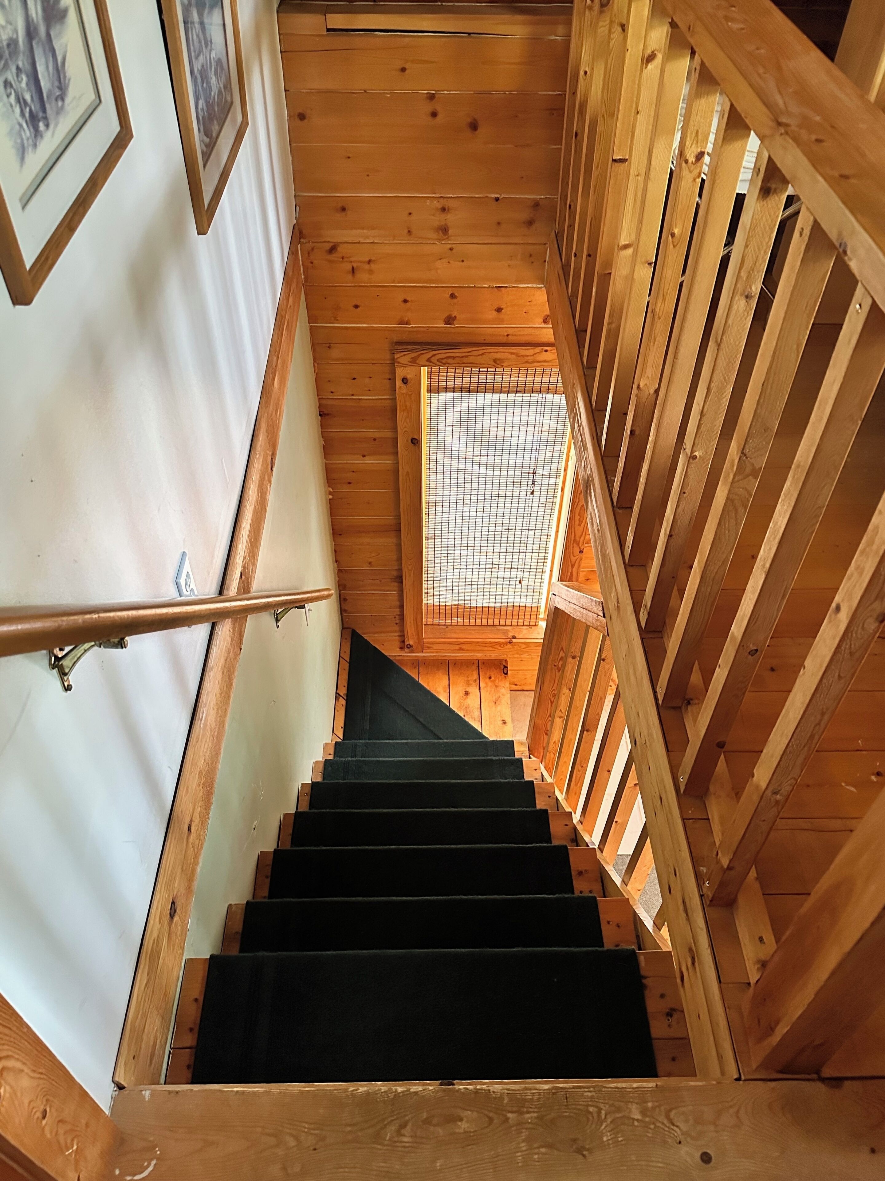 A wooden staircase with a metal handrail, leading to a room with a window and a door.