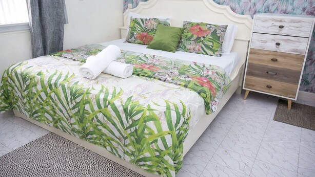 Un letto con lenzuola a motivi floreali, un comodino e un mobiletto con cassetti.