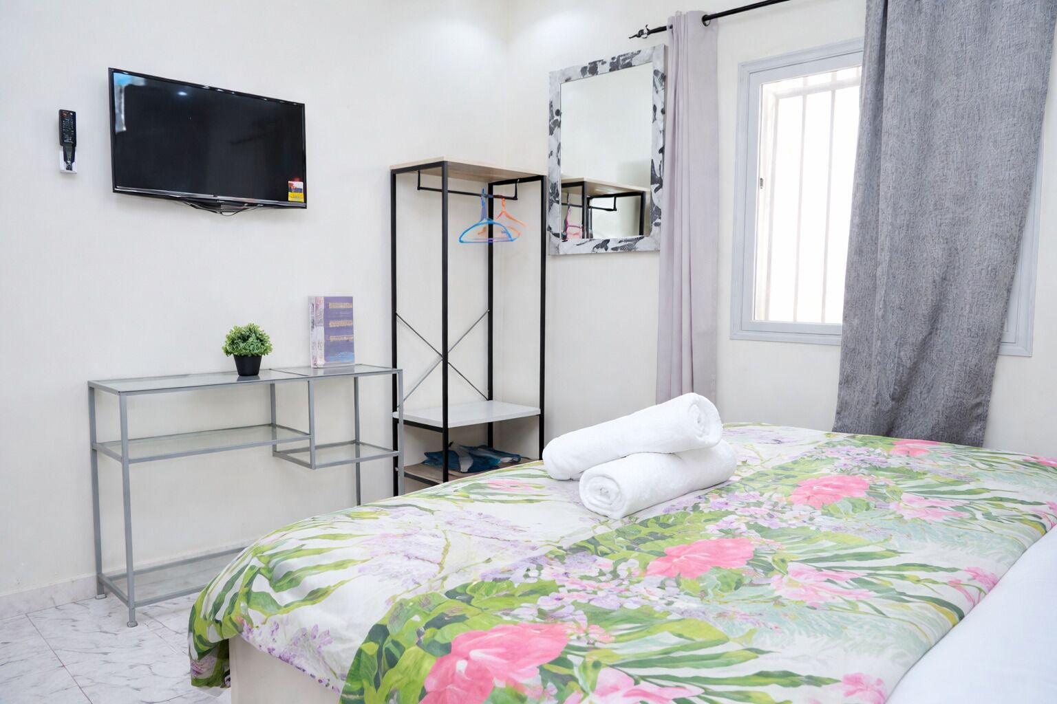 A bedroom with a bed, a TV, a desk with a plant, and a mirror.