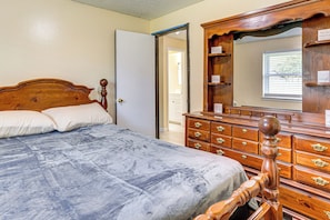 Una camera da letto con un letto di legno, una cassettiera, uno specchio e una porta che conduce in un'altra stanza.