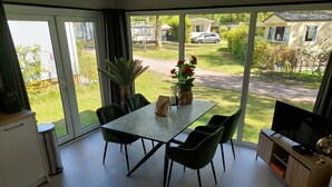 A modern living room with a dining table, green chairs, a TV, and a large window offering a view of a residential area. - Enjoy and relax (Marienberg)