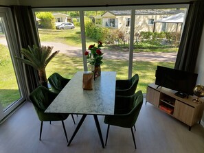 Un espace repas comprenant une table, des chaises, un téléviseur et donnant sur un quartier résidentiel.