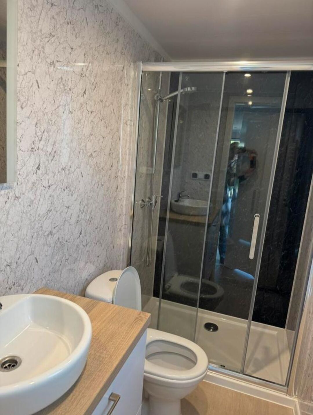 A bathroom with a marble wall, a sink, a toilet, and a glass-enclosed shower.