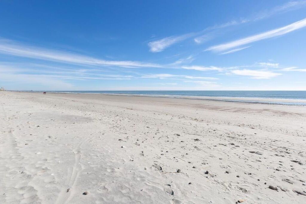 Een breed zandstrand met voetafdrukken en een helderblauwe lucht.