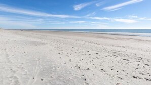 Une vaste plage de sable, parsemée d’empreintes, et un ciel bleu azur.