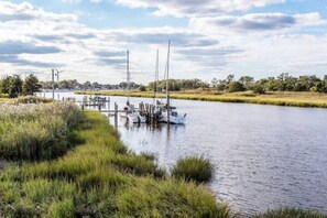 A calm river with boats docked on the left, surrounded by grassy banks and trees in the background.