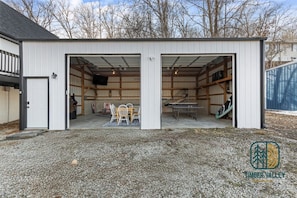 A two-car garage with open doors revealing a dining area with a table and chairs, and a ping pong table. - 5BR Lakefront Home w/ Private Dock & Hot Tub (Sunrise Beach)
