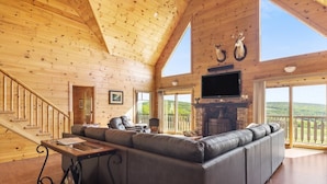Ein Holzblockhaus-Interieur mit einem großen, L-förmigen Ecksofa, einem Kamin und einem an der Wand befestigten Fernseher.