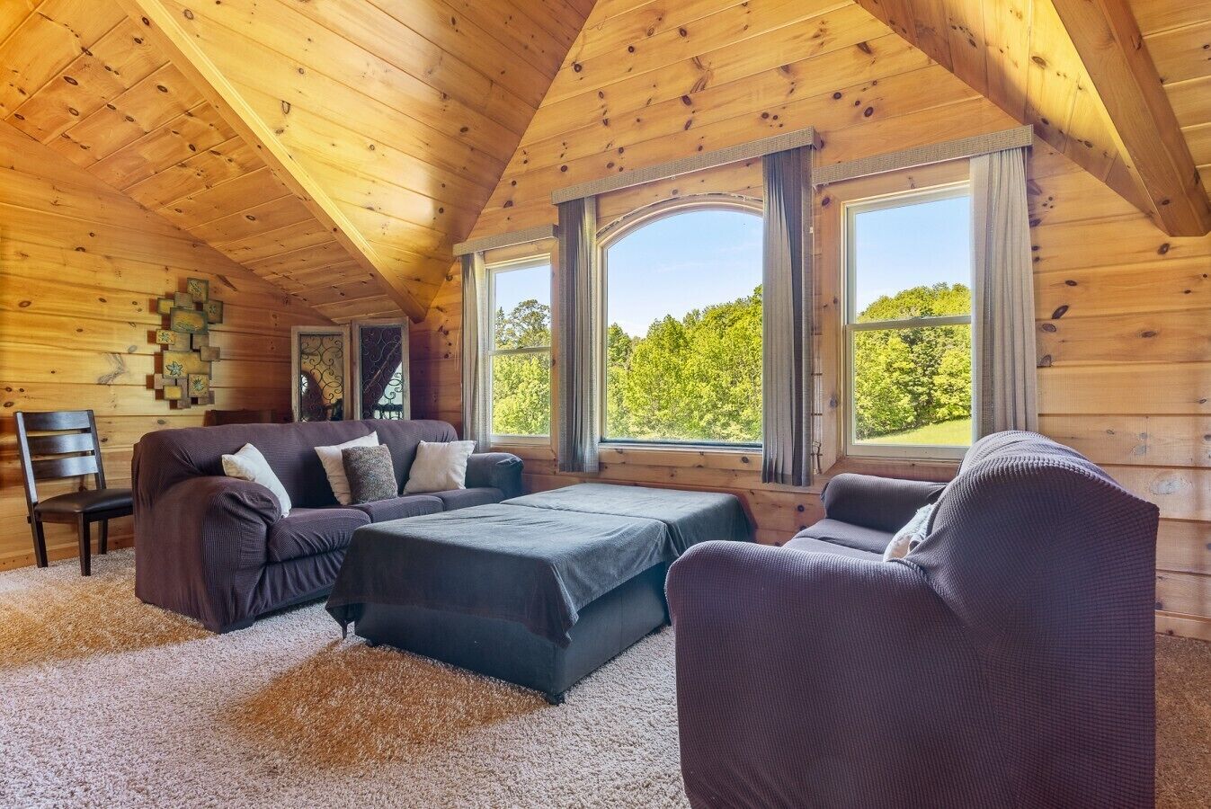 L’intérieur d’un chalet accueillant, avec un plafond en bois, de grandes fenêtres, un canapé, un fauteuil et une petite table.