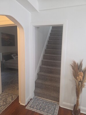 Un escalier recouvert de moquette, dans une pièce où se trouve un tapis à motifs au bas de l’escalier.