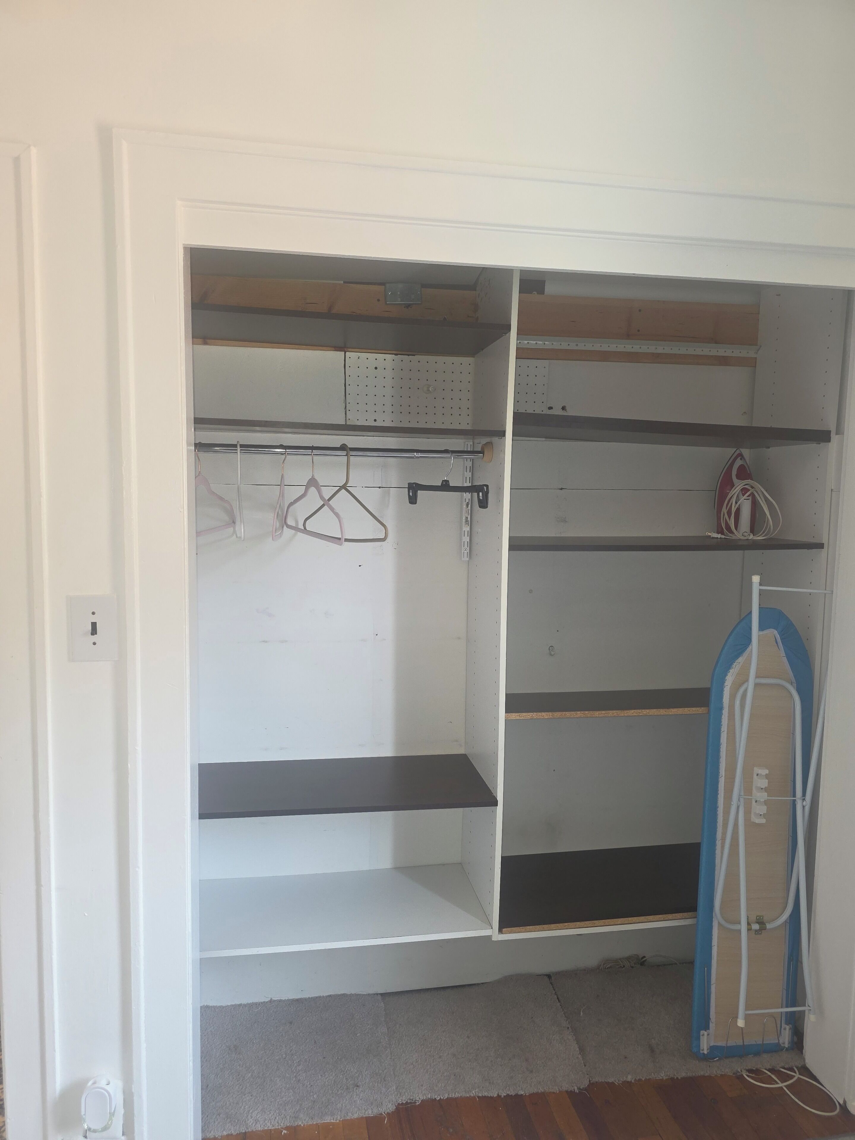 A walk-in closet with open shelves, a hanging rod, and a blue ironing board.