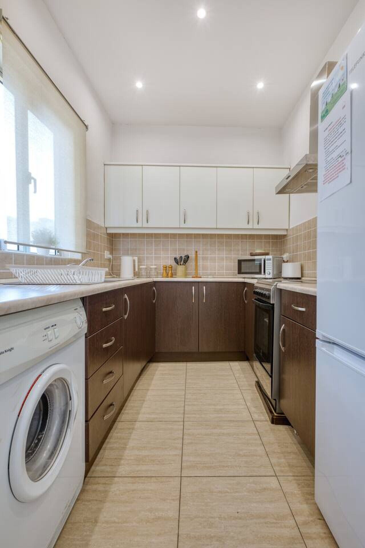 Een kleine keuken met een wasmachine, magnetron, oven en koelkast.