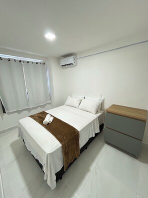 Un dormitorio con cama, mesita de noche, cortinas en la ventana y un aire acondicionado.