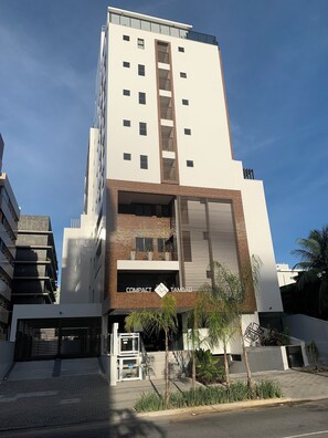 Un edificio moderno de varios pisos con una entrada destacada, una escalera visible y un letrero que dice 'COMPACT TAMBAU'.