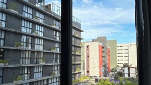 Vista desde una ventana de un edificio de varios pisos con balcones, una zona de estacionamiento y cielo despejado.