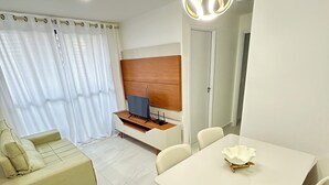 Una sala moderna con comedor, sofá, televisor y cabecera de cama de madera.