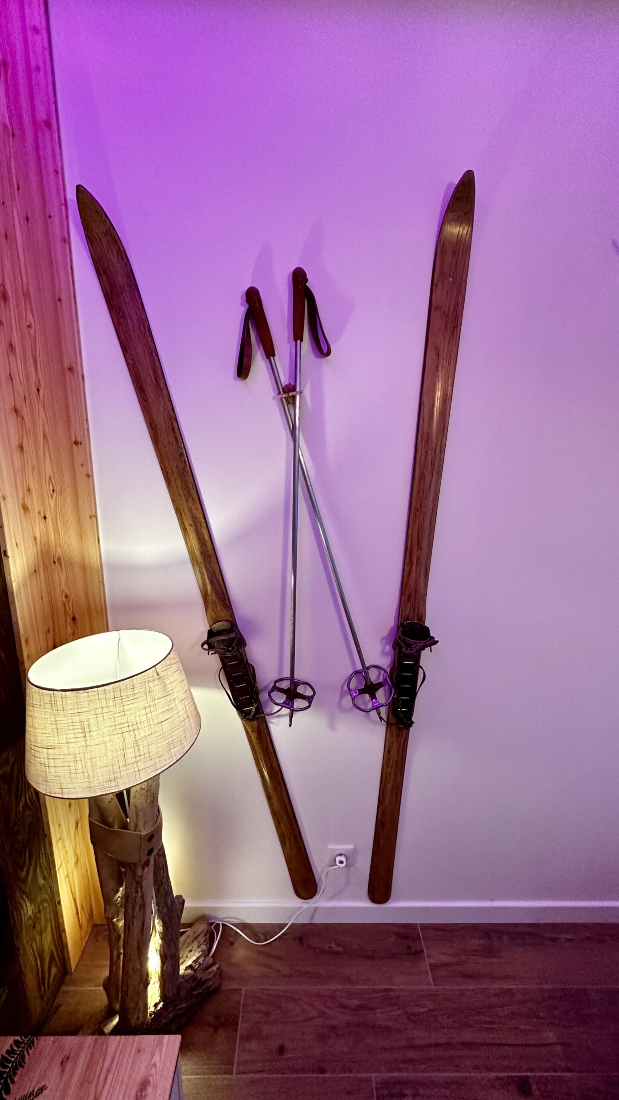 A pair of skis leaning against a wall with a lamp beside them.