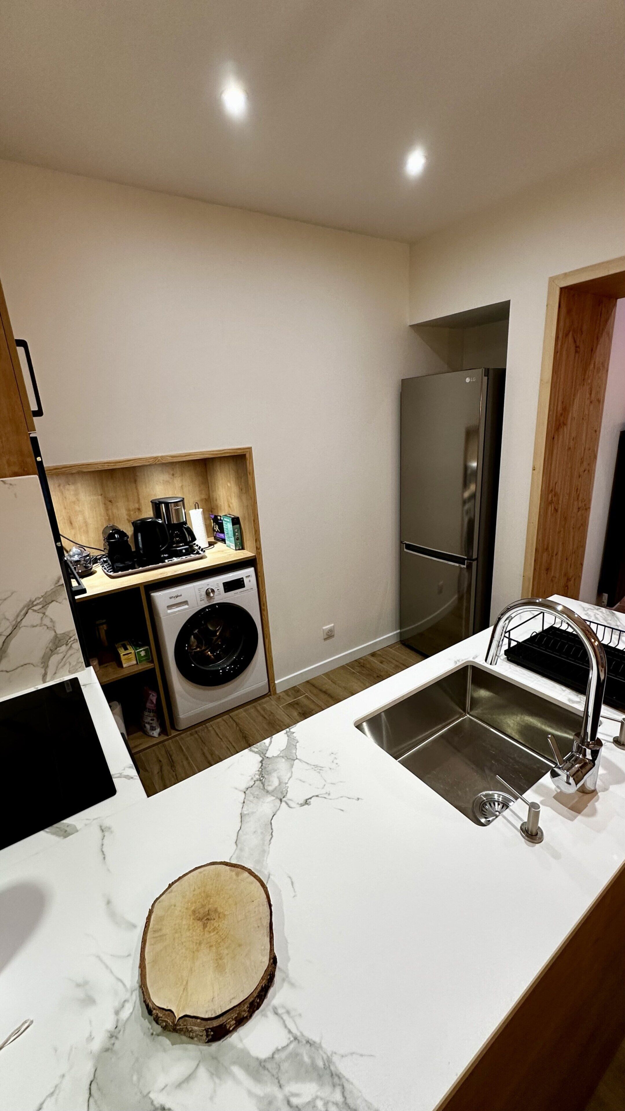 A compact kitchen with a built-in washing machine, a stainless steel refrigerator, and a marble countertop.