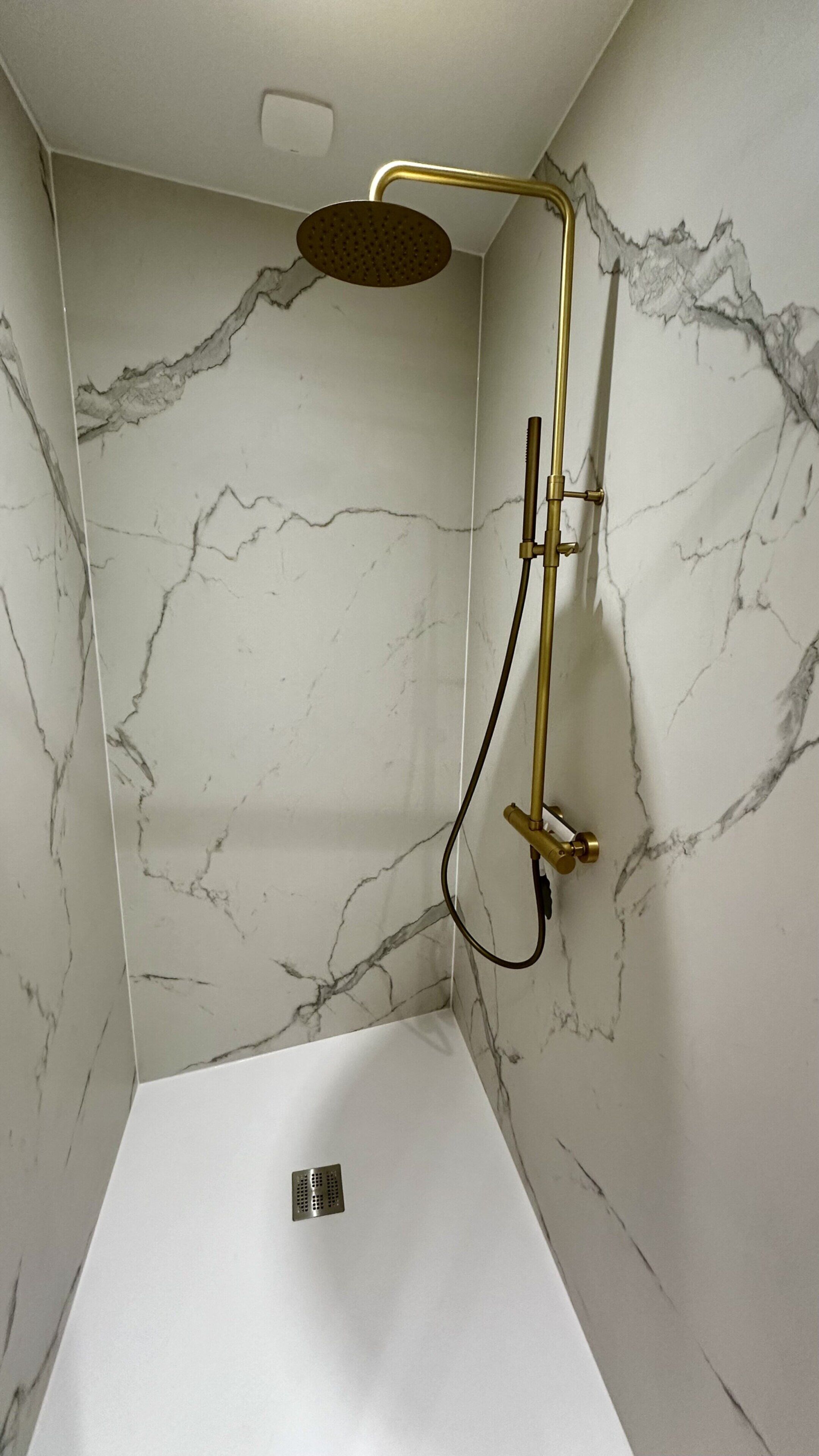 A shower with a gold showerhead and a handheld shower attachment, set against a marble wall.