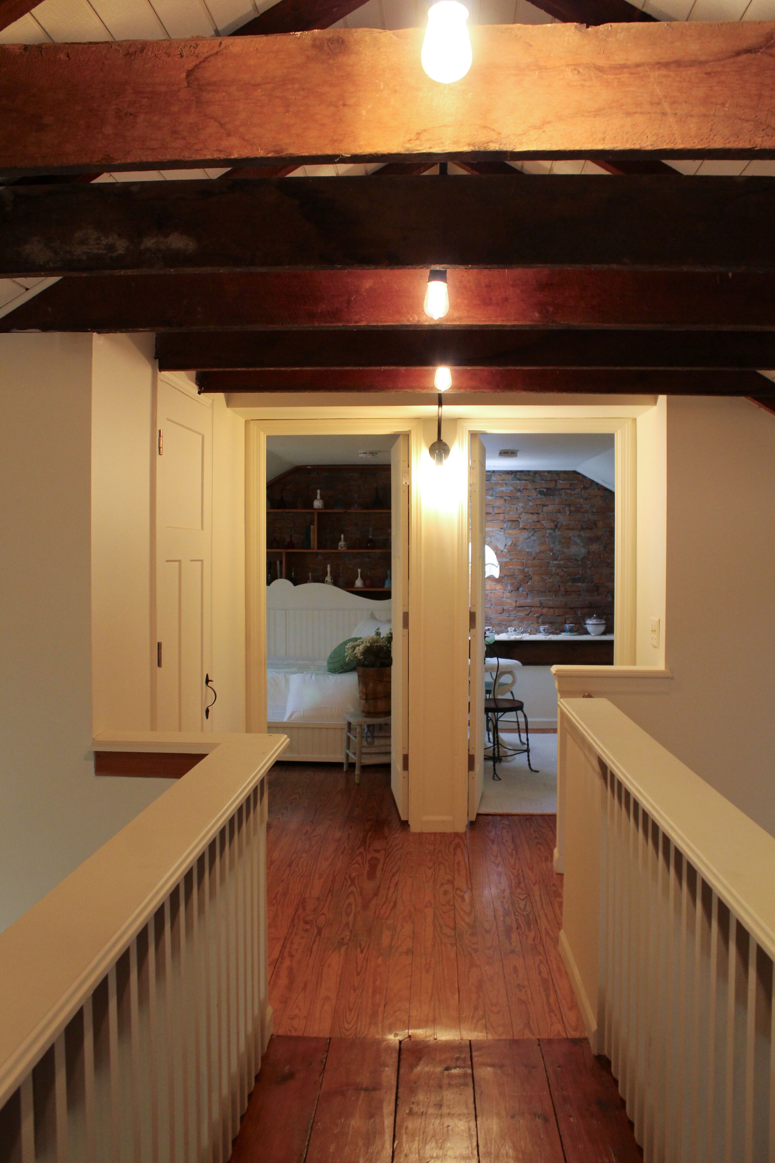 A wooden staircase with a white railing leading to a bedroom with a brick wall and a window.