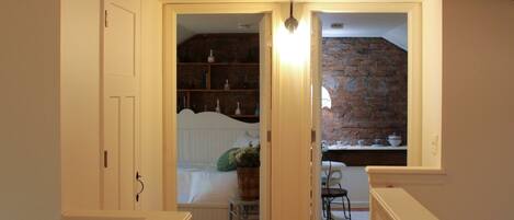 A wooden staircase with a white railing leading to a bedroom with a brick wall and a window.