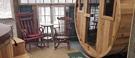 A rustic wooden interior with a large barrel-shaped window, wooden furniture, and a woven rug.