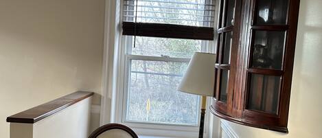 A corner room with a chair, a lamp, a window with blinds, and a wooden cabinet.