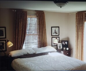 Hotelkamer met een bed, nachtkastje met lamp, fotolijstje en raam met gordijnen.
