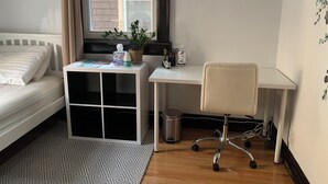 Un dormitorio con cama, escritorio, silla, planta en maceta y ventana.