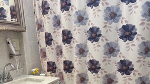 Un baño con lavamanos blanco, un espejo, una alfombra de baño verde y una cortina de ducha con motivos florales.