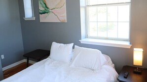 Ein Schlafzimmer mit Bett, Nachttisch, Lampe, Fenster und einem Bild an der Wand.
