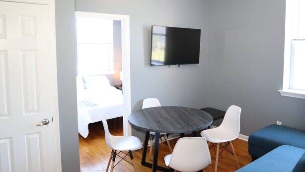 Ein Zimmer mit rundem Tisch, vier Stühlen, einem Flachbildfernseher, einem Bett und einem Fenster.