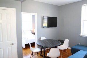 A room with a round table, four chairs, a flat-screen TV, a bed, and a window. - Modern 1BR/1BA Apartment - Self Check-In (Belleville)