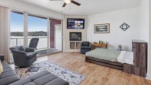 Et værelse med en seng, et skrivebord, en stol, et fjernsyn og en balkon med udsigt.