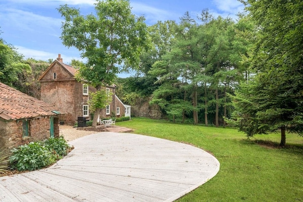 A stone house with a wooden deck and a grassy yard.