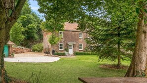A rustic brick house with a well-maintained lawn and a picnic table in the foreground. - Idyllic Waterside Georgian Cottage (Halberton)