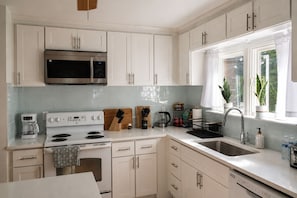 A modern kitchen with white cabinets, a stainless steel microwave, a stove, and a sink.