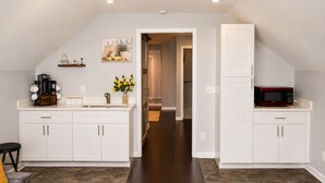 A modern kitchen with white cabinetry, a coffee maker, a microwave, and a decorative plant.