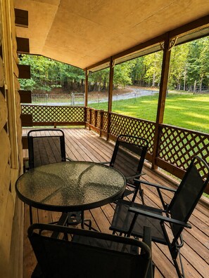 A covered outdoor deck with a glass table and chairs, surrounded by a wooden fence and greenery.