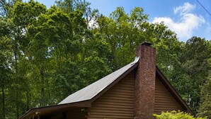 A log cabin with a porch, a chimney, and a small tree in the yard.