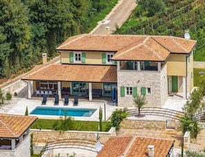 A two-story stone building with a swimming pool, outdoor seating, and a view of a vineyard. - Elegant Family Retreat With Pool in Istria (Zminj)