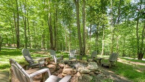 Un terrain de camping équipé de chaises Adirondack et d’un foyer, le tout entouré d’arbres.