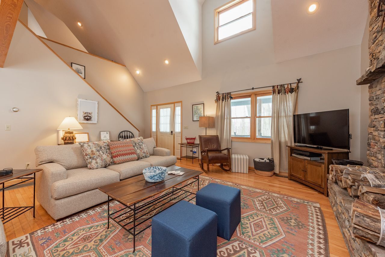 A spacious living room with a high ceiling, a sofa set, a coffee table, a television, and a fireplace.