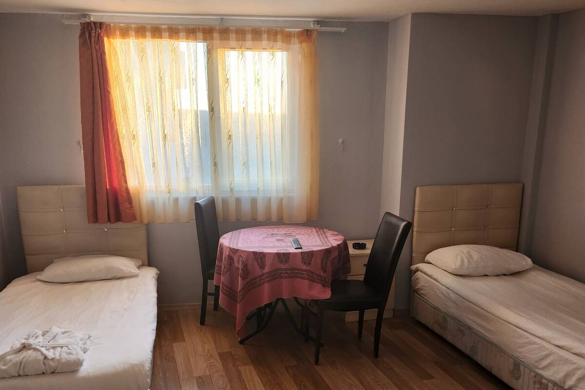 A room with two single beds, a small round table with chairs, and a window with sheer curtains.