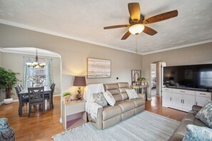 Ein Wohnzimmer mit Sofa, Fernseher, Deckenventilator, Esstisch und Stühlen.